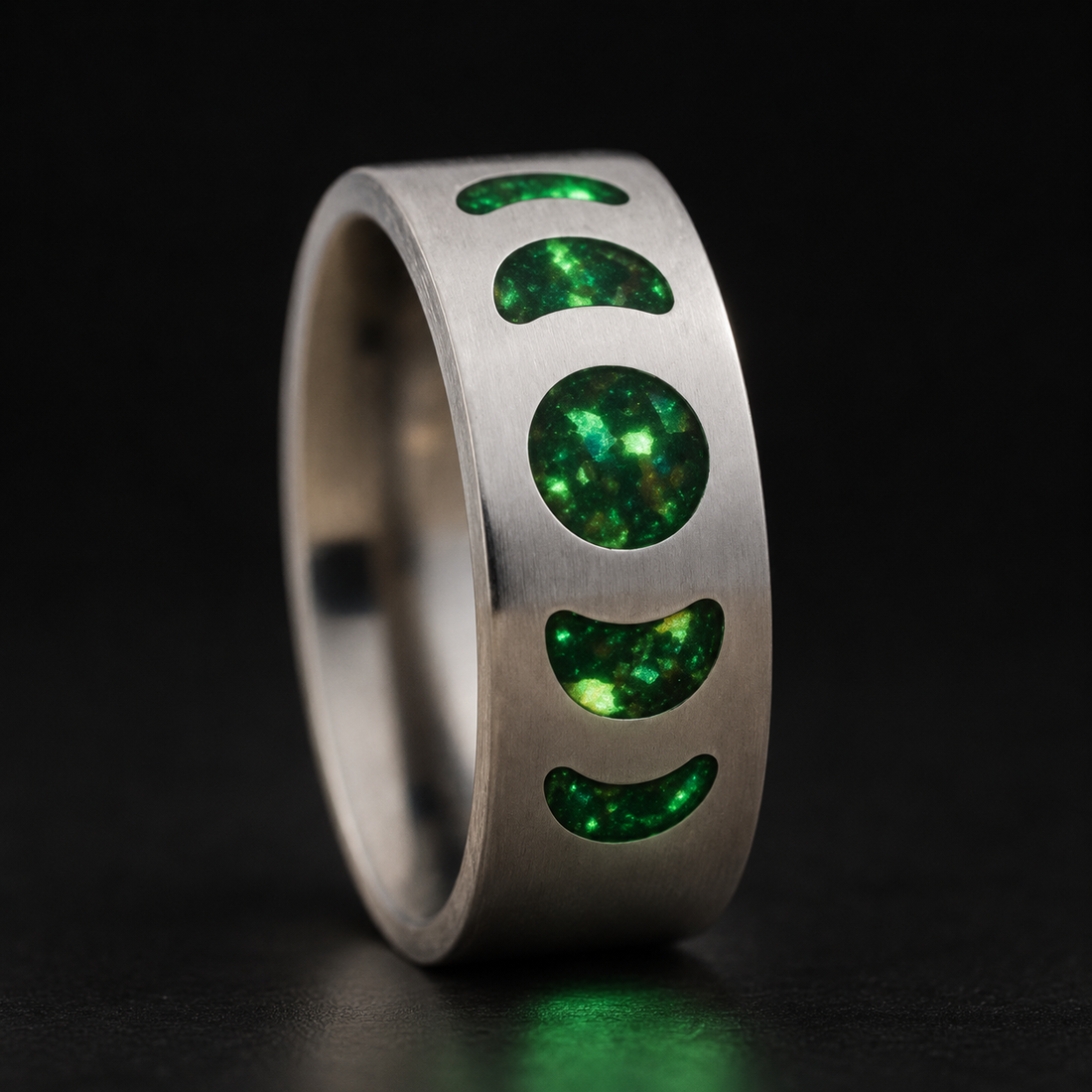 Moon Phase Vulcan handcrafted titanium ring with green glowing moon phase inlays on a dark background